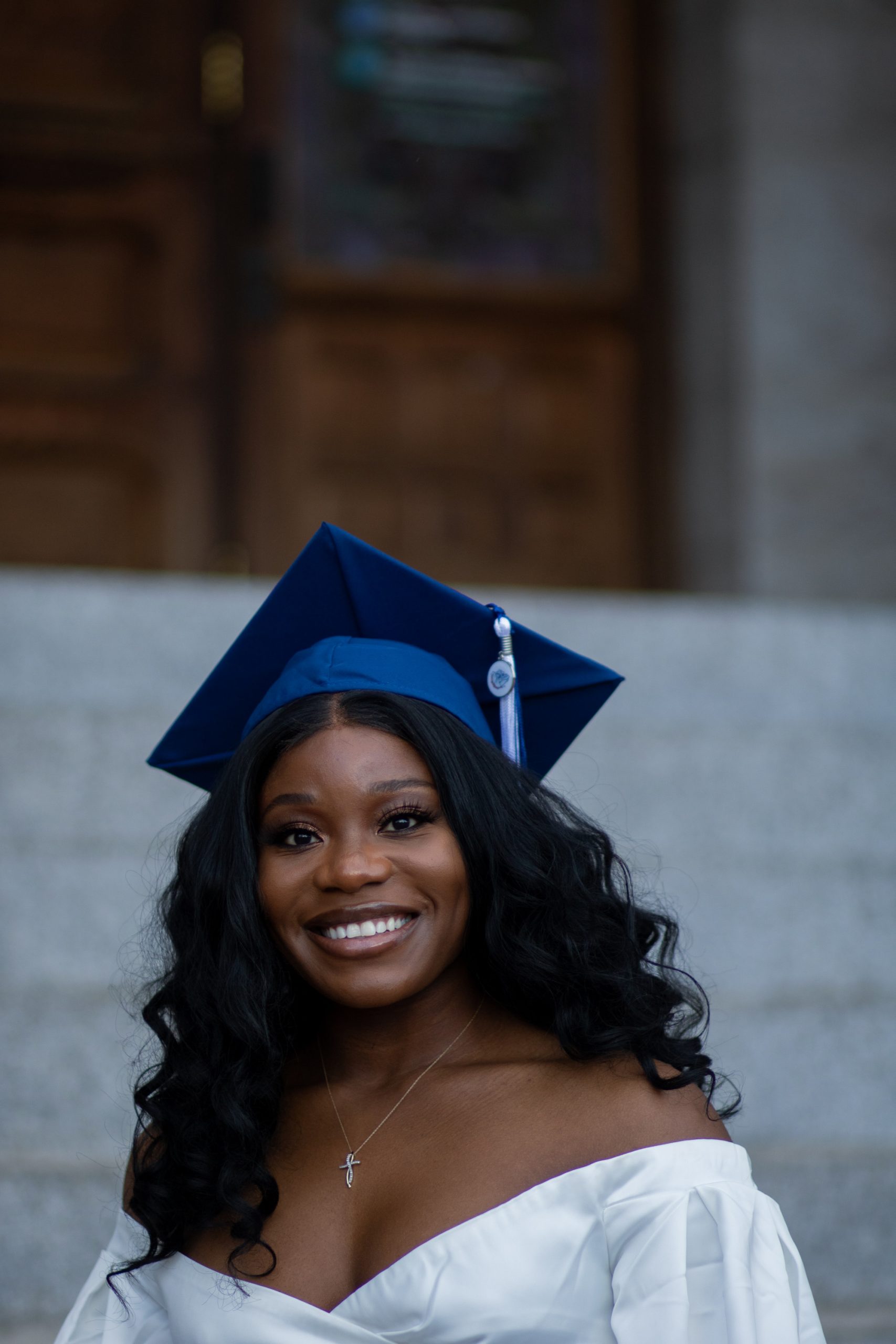 Woman smiling in front of University building with graudation cap and gown on.